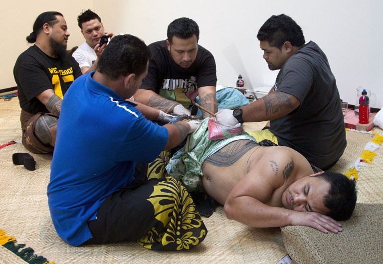 Ricky Masoe (bottom R) lying down as assistants (L) hold his skin tight while master tattooist Su'a Paul Sulu'ape (R) uses a traditional method to tattoo him. ©AFP