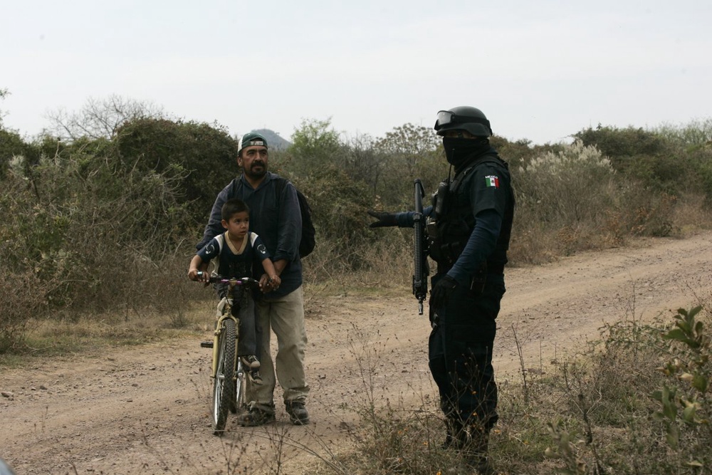 A police officer stops a man and a young boy riding on a bike near a site where homicide experts are recovering bodies buried in a mass grave in Tlajomulco de Zuniga. ©Reuters/Alejandro Acosta 