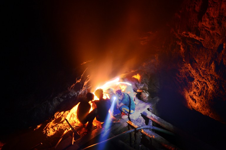 Indian coal miner, Surya Limu (inside hole), squats with other miners by a fire to keep warm hours before dawn. ©AFP