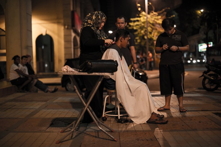 Azmina Burhan (L) cutting the hair of a homeless person in downtown Kuala Lumpur.