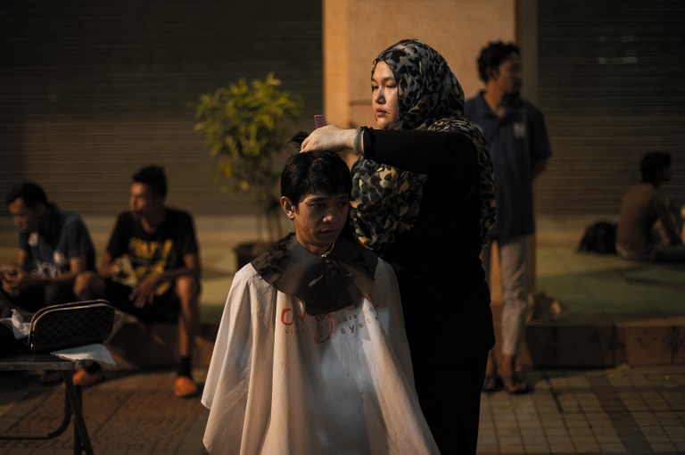 Stylist Azmina Burhan (L) cutting the hair of a homeless man in downtown Kuala Lumpur. ©AFP