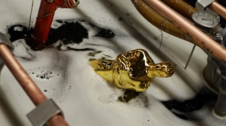 An Oscar statuette is dipped in an electrically charged tub as it is plated with gold at the R.S. Owens factory. ©AFP 