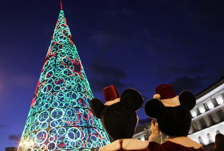 Two people dressed as Mickey Mouse stand next to a Christmas tree made out of lights as they wait to perform for children in Madrid, Spain. ©Reuters/Susana Vera