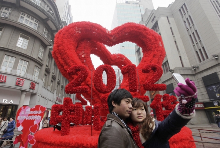 A couple takes a photograph with a mobile phone in front of a red heart decoration on the Valentines Day in Wuhan. ©REUTERS/Darley Shen