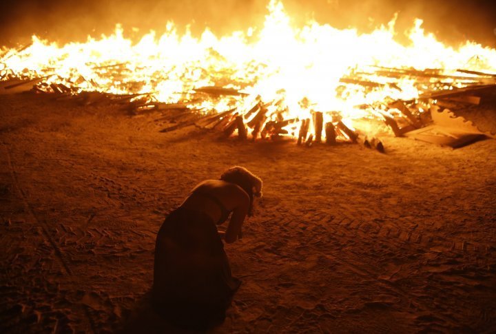 A Burning Man participant kneels as she pays homage to the Temple of Whollyness while it burns. ©REUTERS