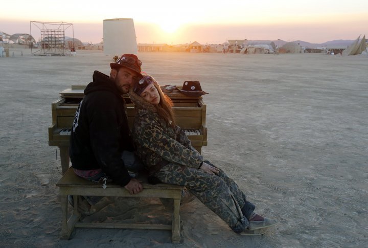 A couple rest at a piano at a desert art installation at sunrise.  ©REUTERS