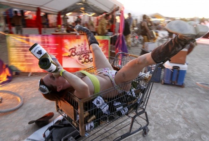 A participant who goes by the playa name "Honey B" drinks from bottles of champagne as she lies atop empty bottles in a shopping cart during the "Gold Bikini Happy Hour" hosted by Rat Camp. ©REUTERS