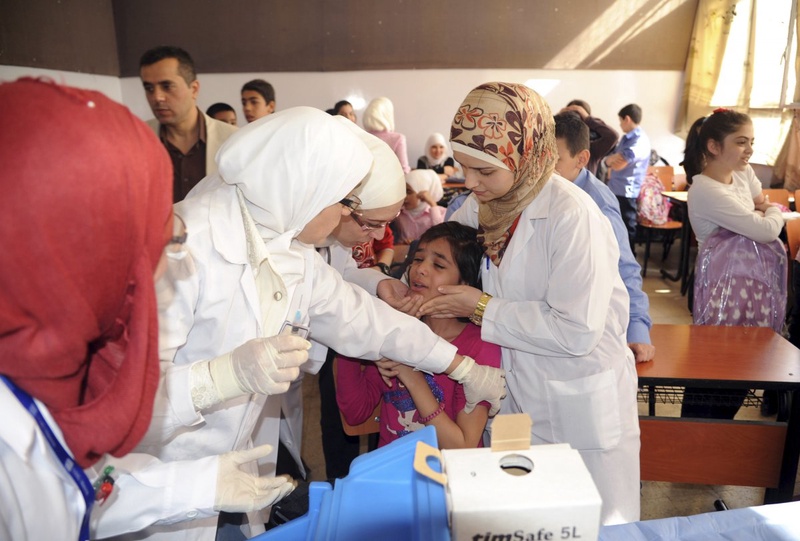 Syrian health workers administer polio vaccination to a girl at a school in Damascus. ©Reuters