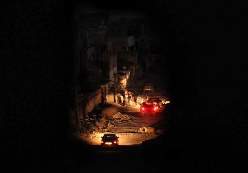 A picture taken through a hole in a wall shows cars driving at night past damaged buildings in the city of Benghazi following fierce fighting with armed groups including Islamic State (IS) jihadists. 