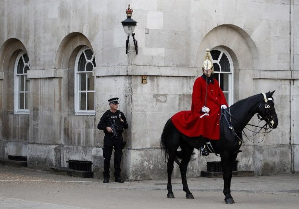 An armed British police officer (L) holds his automatic weapon as he stands on duty whilst a member of the The Life Guards sits on his horse during the Changing the Guard ceremony on Horseguards Parad