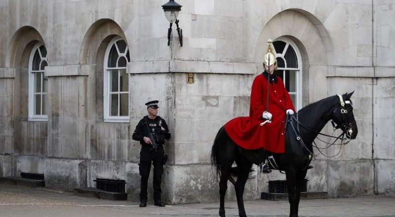An armed British police officer (L) holds his automatic weapon as he stands on duty whilst a member of the The Life Guards sits on his horse during the Changing the Guard ceremony on Horseguards Parad